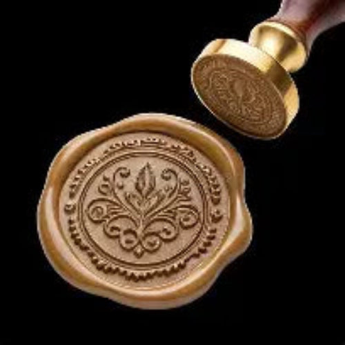 Brass wax seal stamp with wooden handle shown alongside a gold wax seal impression featuring intricate floral botanical design, for wedding invitations and luxury stationery